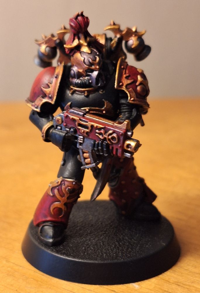 A space marine wielding a bolter, whose armor is red and black with gold accents. Atop its head is a big ol' red tassle.