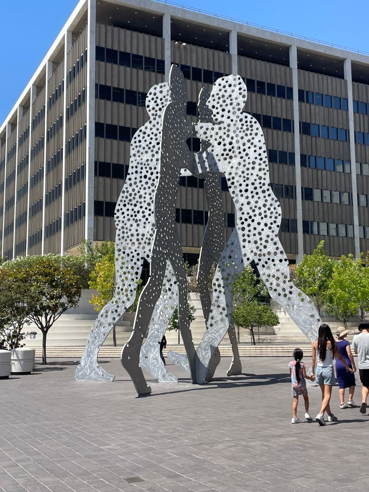 Massive sculpture DTLA showing 4 steel cutout person shapes pushing against each other and covered in small holes 