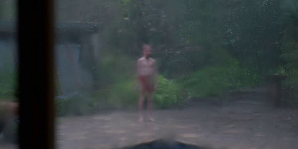 A imagem do "Oliver" ensanguentado através do vidro. Ela está sendo distorcida pela água da chuva que está escorrendo no vidro.