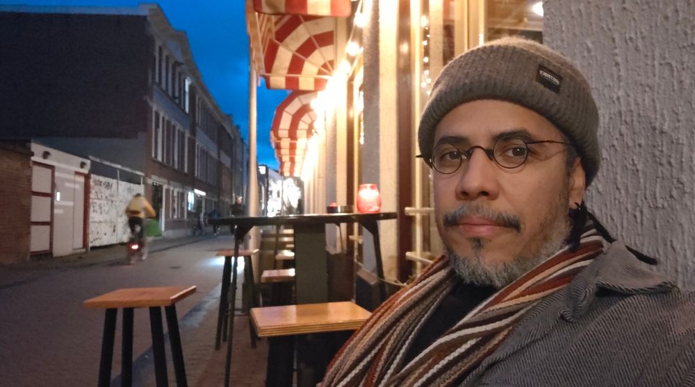 A weird ass dude with salt and pepper beard with a ridiculous gray beannie with a lighted street