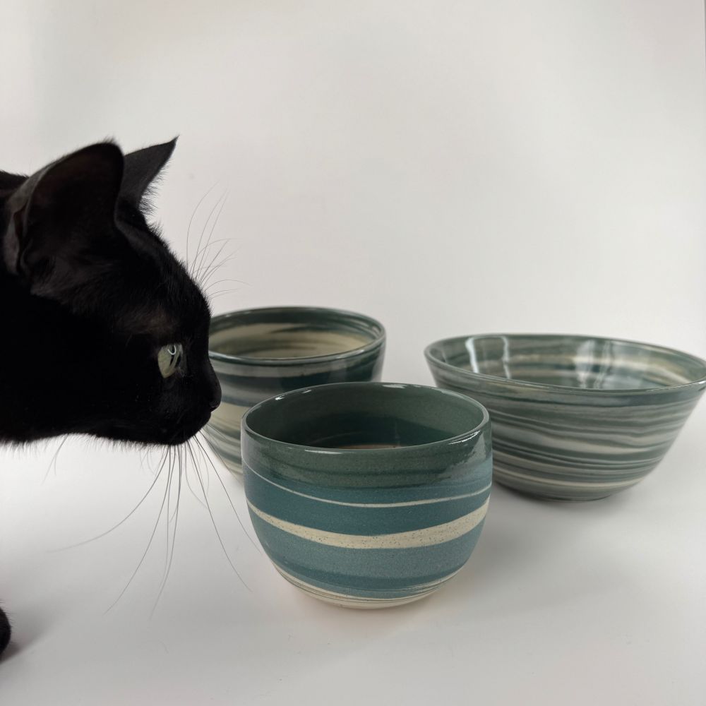 Three marbled pots on a white background with black cat on the left of the image, sniffing the pot.