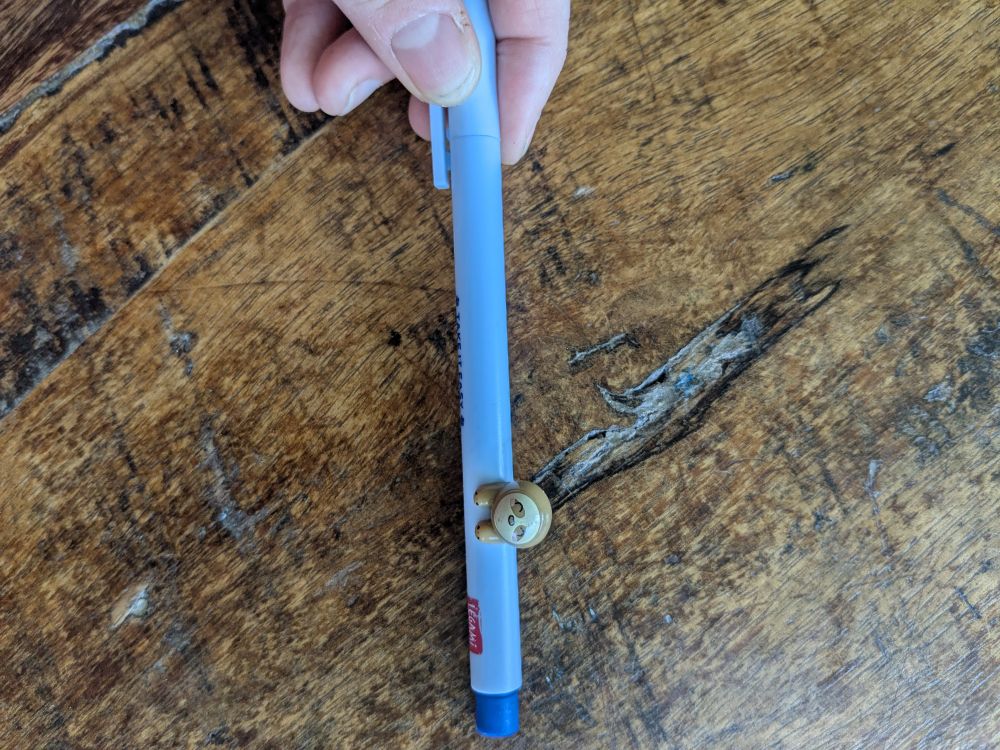 Stylo bleu avec une petite figurine de paresseux ( aussi appelé Aï) dessus 