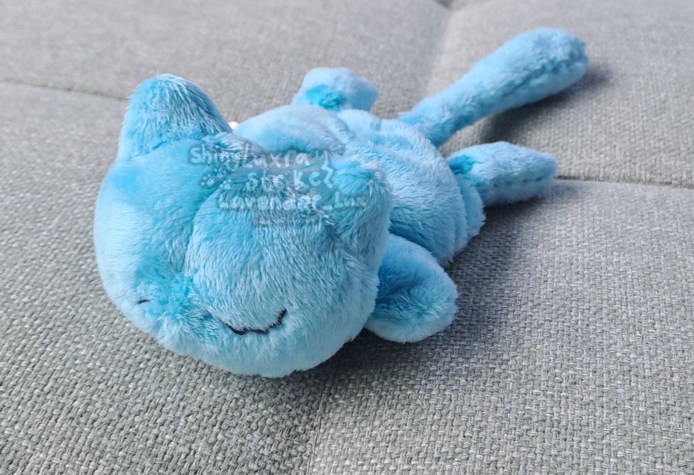 Shiny blue sleepy Mew beanie as seen from the front/side, lying on my pastel green couch.