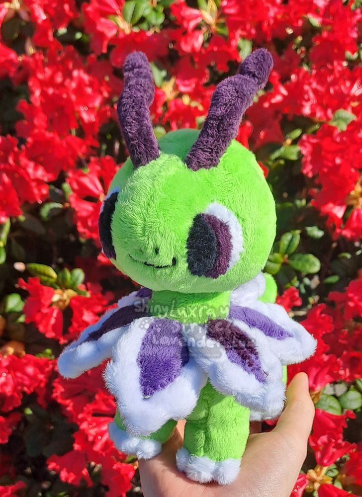 A custom shiny Meganium chibi plush I made for a comm, held up in front of red flowers. Base pattern belongs to Syleniscrafts, w some edits by me