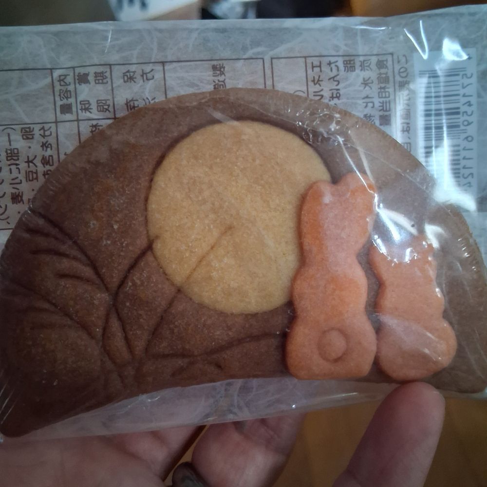 A brown semi circle cookie with a light brown full moon and two small orange bunnies looking at it.