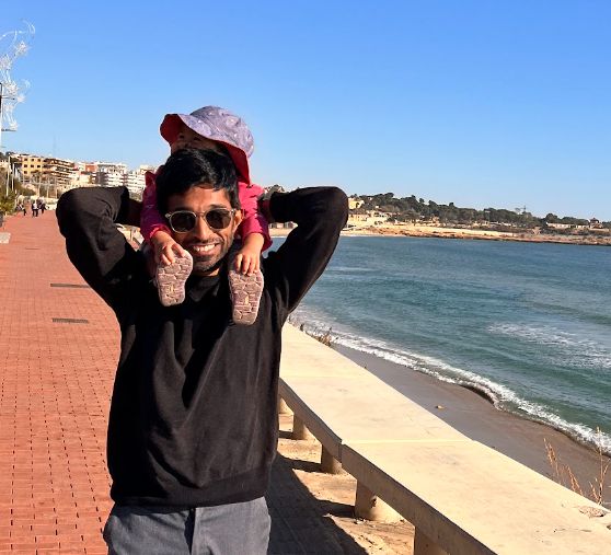 Me wearing a sweater walking alongside a beach with a small child on my shoulders.