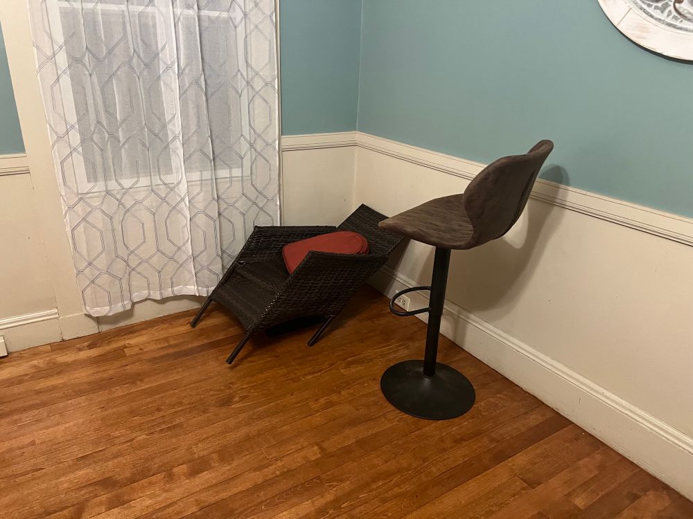 A woven chair, bent in a parallelogram shape, with a stool next to it facing it.