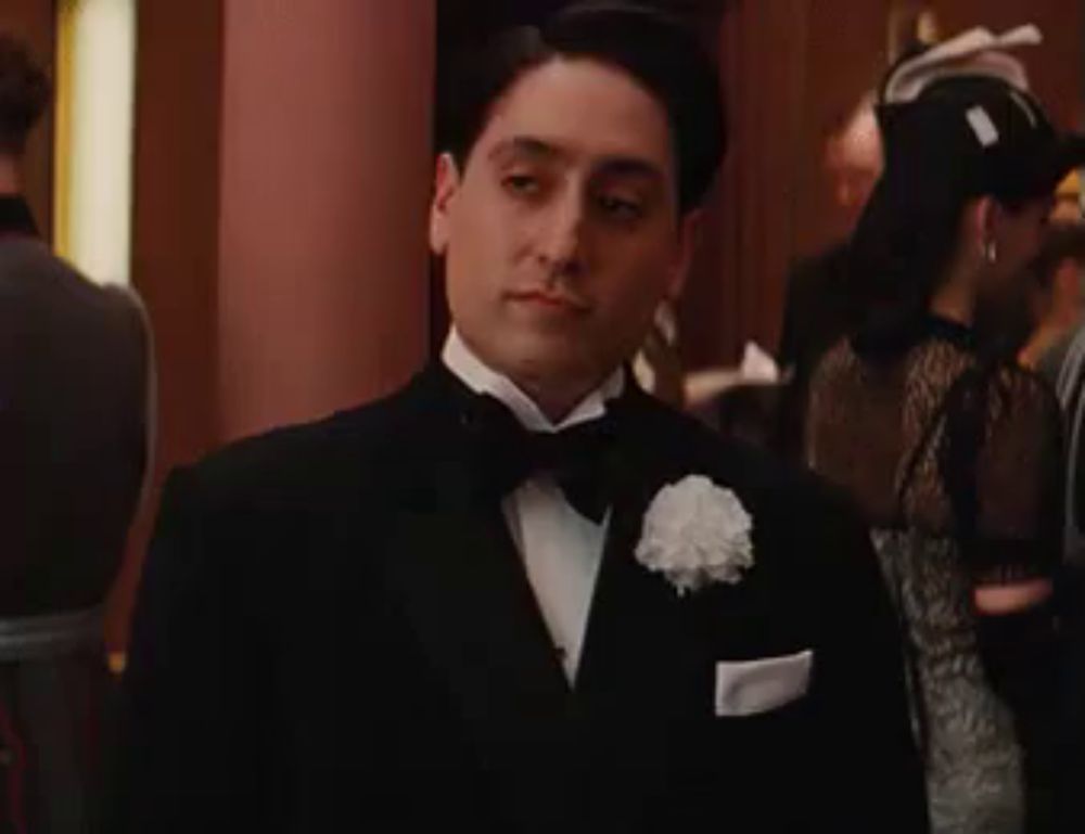 a man in a tuxedo and white gloves is looking at something .