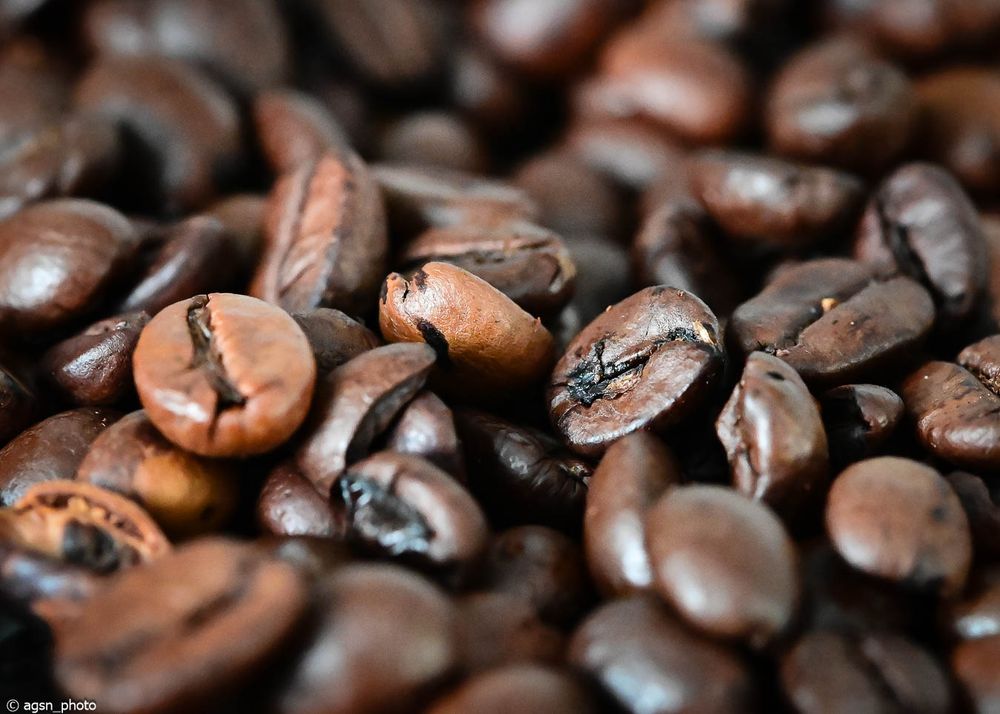 Nahaufnahme von gerösteten Kaffeebohnen mit sichtbaren Rissen und glänzender Oberfläche. /
Close-up of roasted coffee beans showing cracks and shiny surfaces.
