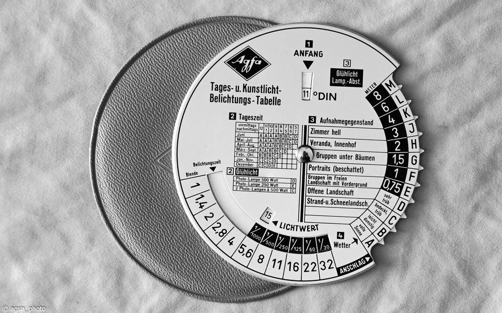 Eine runde Einstellungstabelle als Hilfe für die richtige Belichtungszeit und Blende bei Tages- oder Kunstlicht, ähnlich einer Parkscheibe.
Gefragt wird nach der Filmempfindlichkeit, Tageszeit und Abstand zum Motiv. Danach lässt sich eine Blende/Zeit-Kombination ablesen.