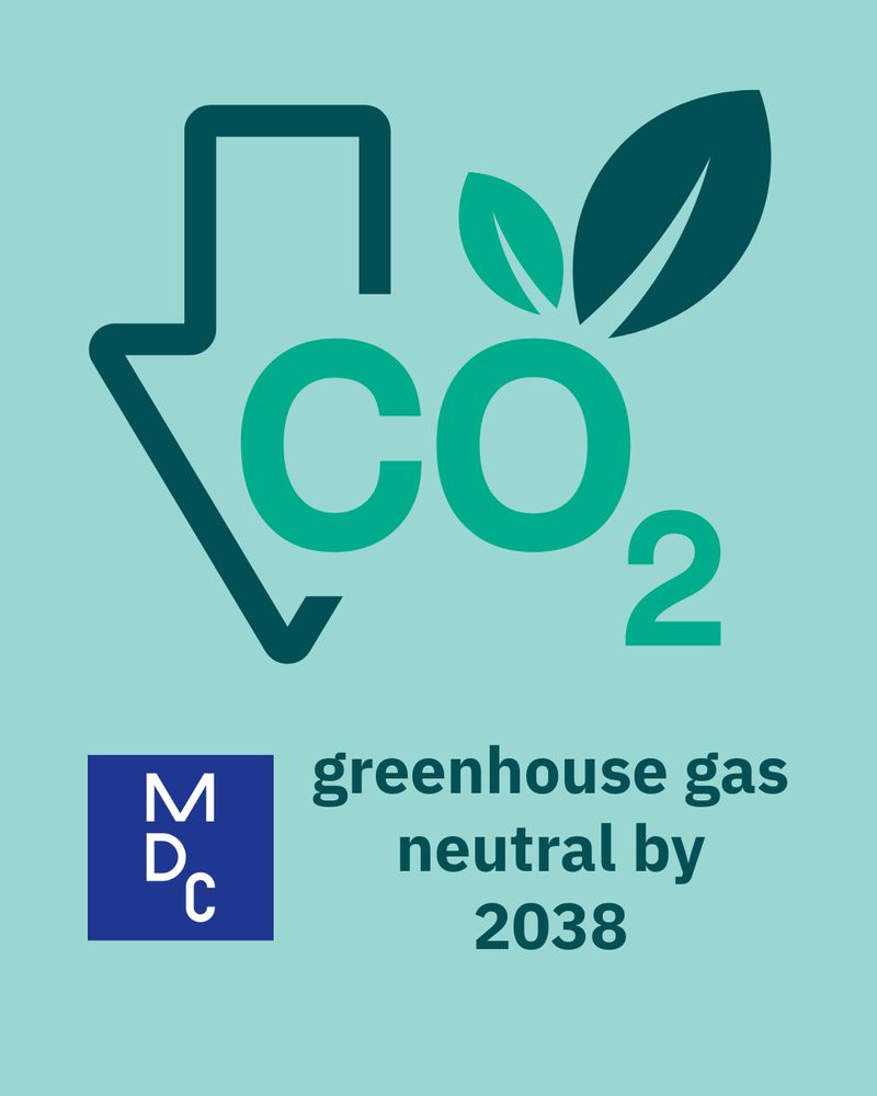 Graphic with icon and text: A stylized CO₂ symbol with a downward arrow and green leaves appears in the upper half of the graphic against a pale teal background. The overlaid text at the bottom is in bold dark green sans-serif font and reads, “greenhouse gas neutral by 2038.” A blue logo of the Max Delbrück Center is positioned in the lower left corner.