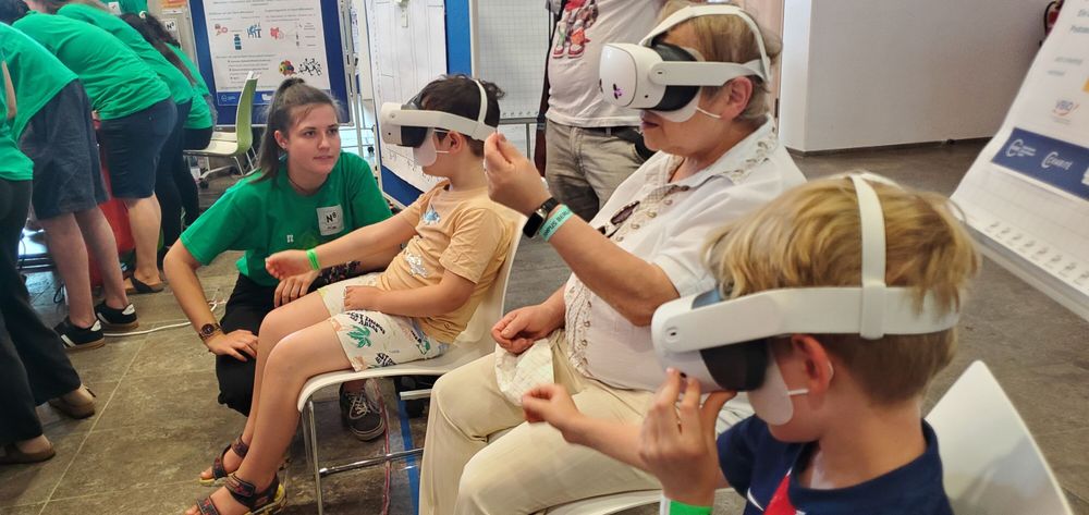 People of different ages using VR headsets at a tech event, with a guide explaining nearby.