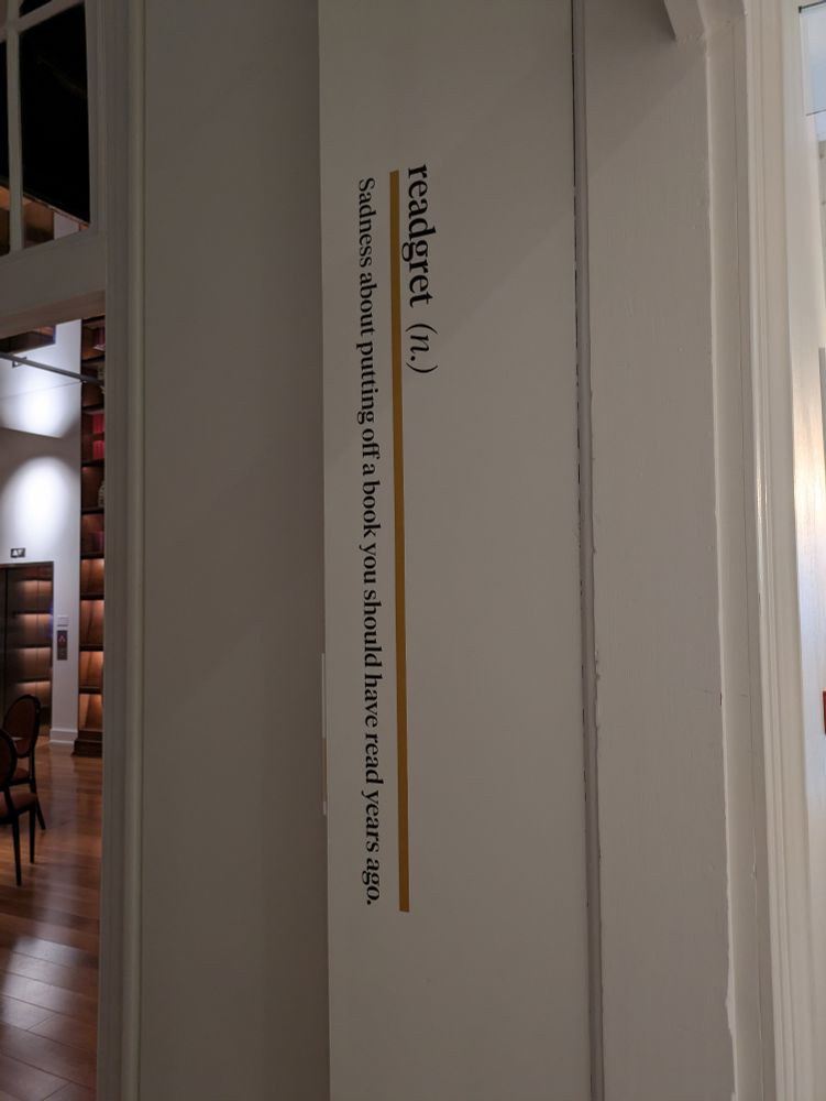 A word and definition printed on the inside of a door jamb. The word is readgret. It means sadness about pushing off a book you should have read
