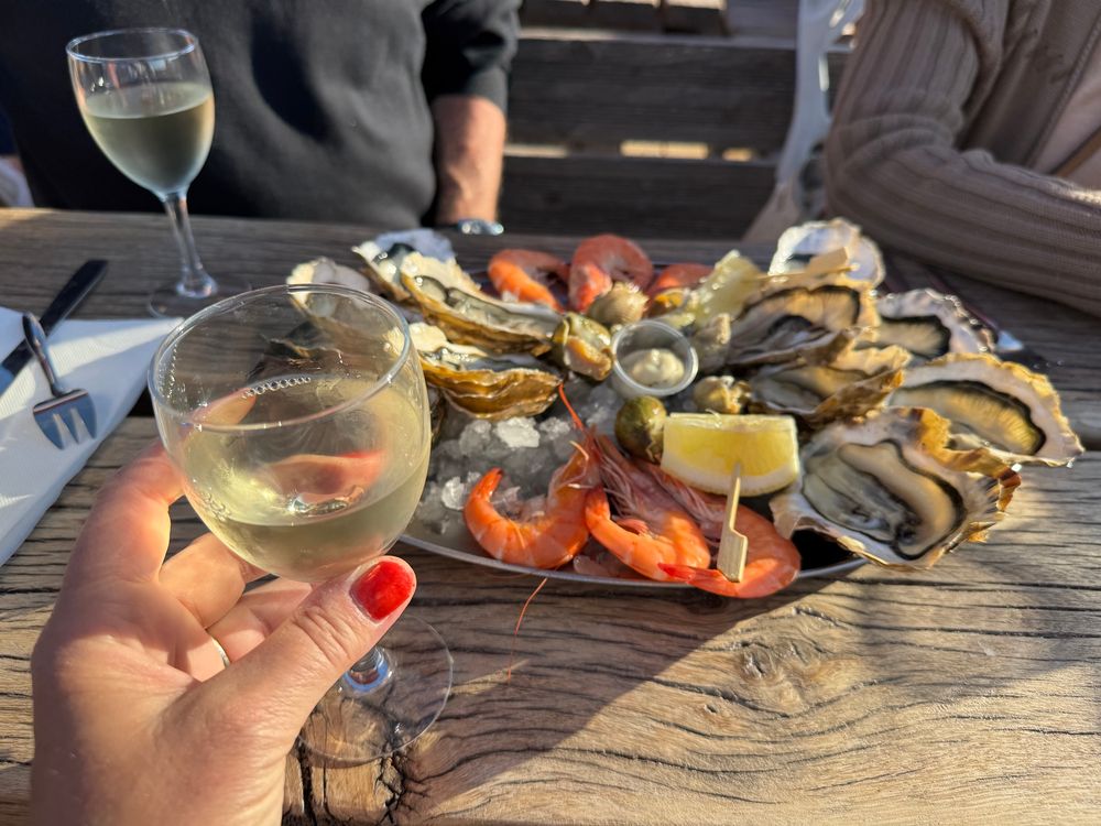 Plateau d’huîtres crevettes et bulots avec ma main qui tient un verre de vin blanc 