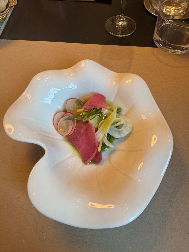 Assiette en forme de corolle blanche avec légumes de toutes les couleurs : petits pois fenouil tranches de radis de couleur sur pesto vert 