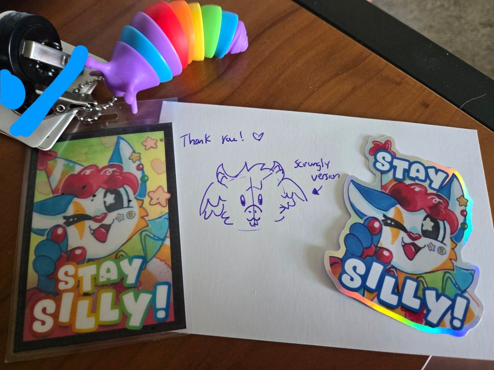 A picture of my matching badge and sticker of a colorful clown cat with rainbow text that reads "Stay Silly!" Between the badge and sticker is a "scrungly" doodle of my character Toybox.