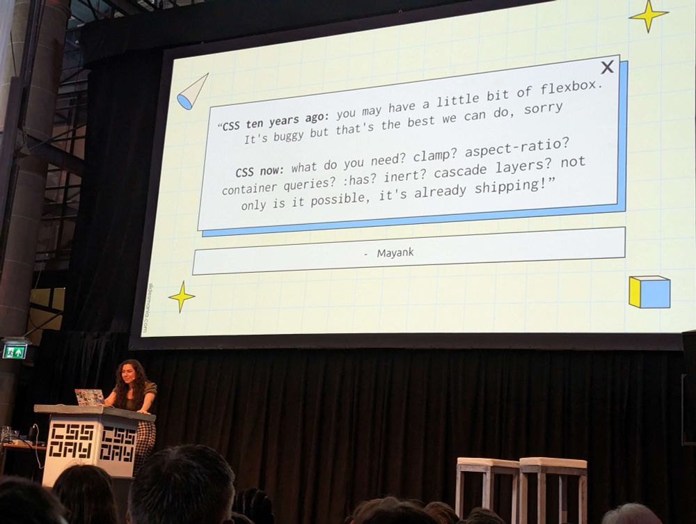 a woman on stage, Una Kraveys, standing behind a podium, behind her projected into the screen is the tweet from Mayank