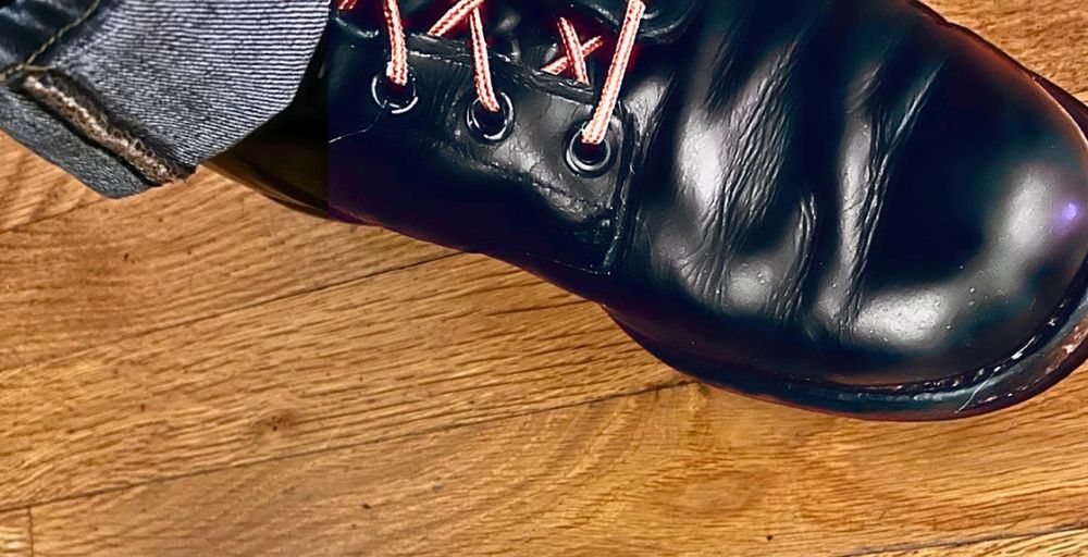 Close-up of a black combat boot on a hardwood floor.
