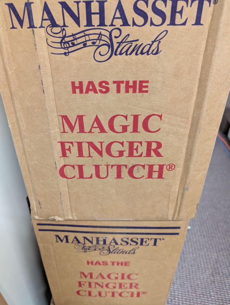 A cardboard box of Manhasset music stands with the label "has the magic finger clutch" printed in red on the side of the box