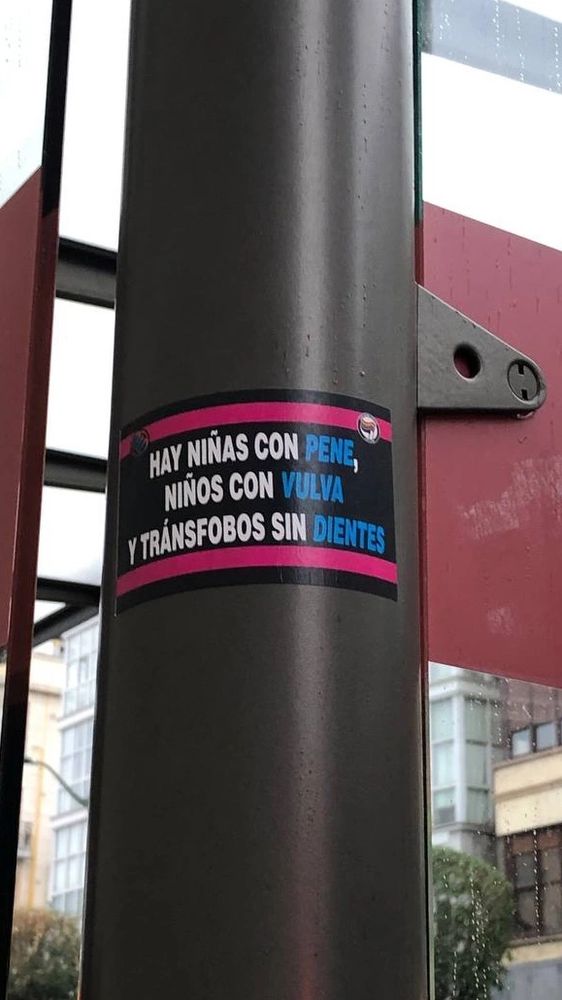 spanish language sticker on a pole that reads, "there are girls with penises, boys with vulvas, and transphobes without teeth"
