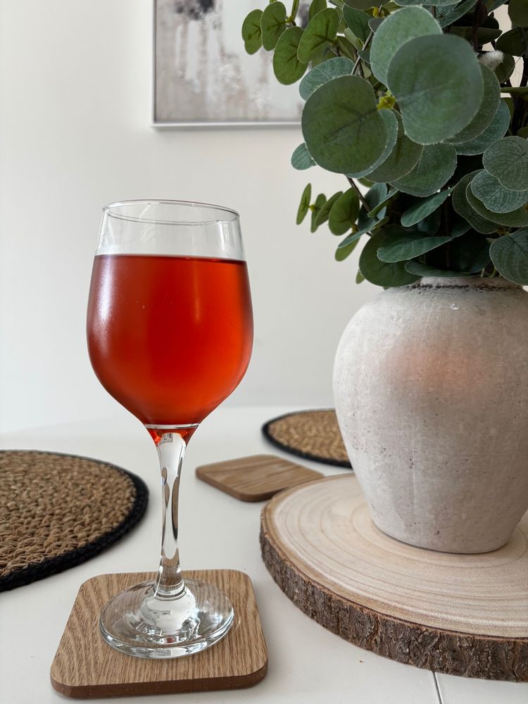 A glass of rosé wine on a wooden coaster with a plant sat next to it on a table. 