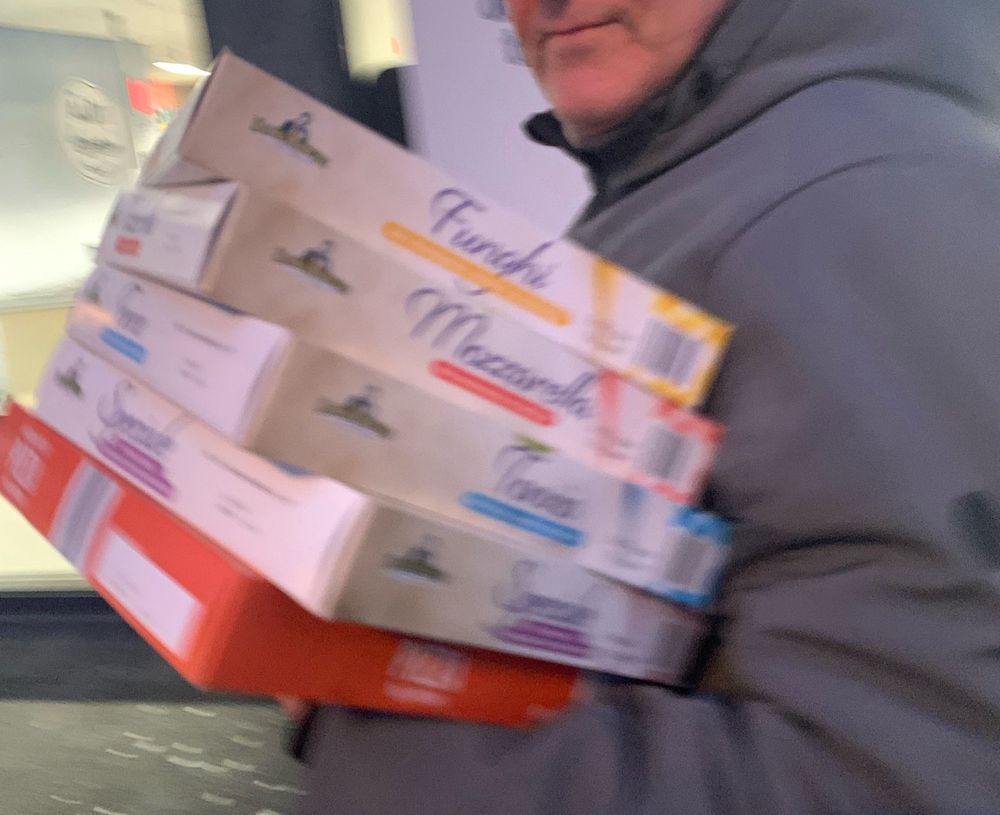 Iets onscherpe foto van mijn man in grijze jas, die vijf dozen bevroren pizza’s vasthoudt 