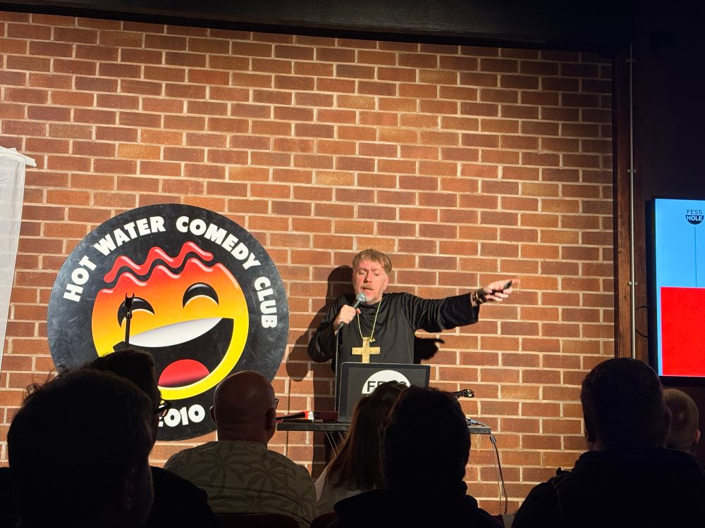 Fess hole live in Liverpool with shit emoji hot water comedy club logo on the wall.