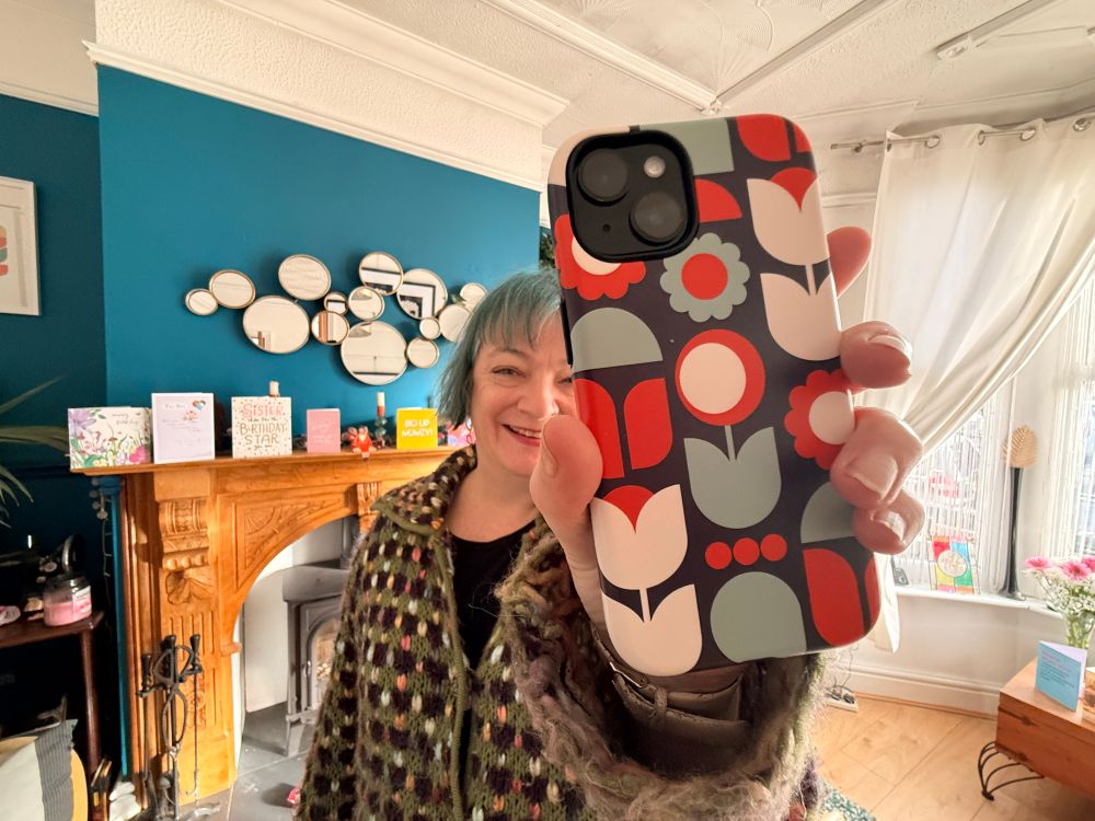 A woman holding up a nicely patterned phone case in a living room.