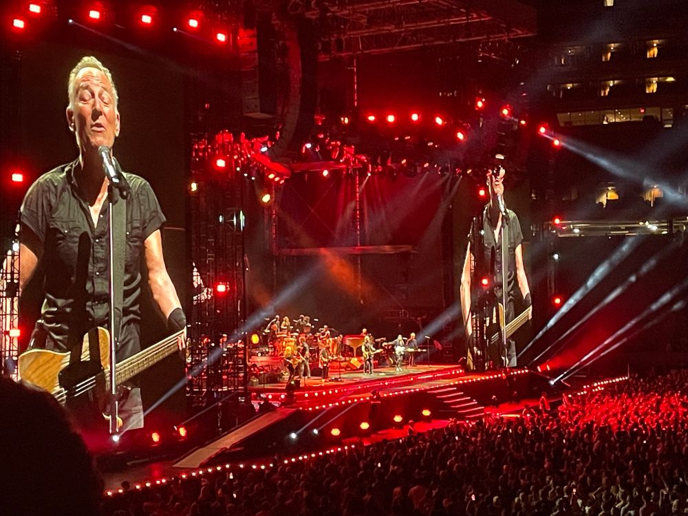 Landscape shot of Bruce Springsteen performing at MetLife Stadium with red stage lighting.