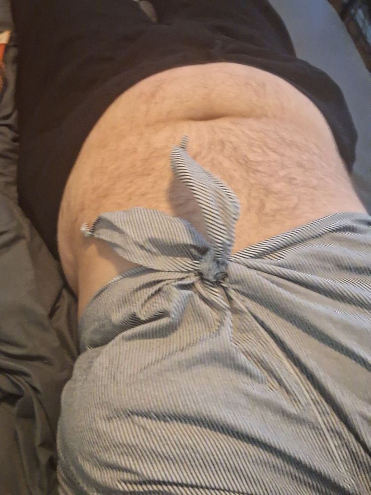 Photo focused on my torso and thighs. I'm lying on my back on dark gray sheets wearing a black and white vertically striped crop top that ties in front. I am also wearing black sweatpants. My midriff (which is hairy, pale, and soft) is showing.