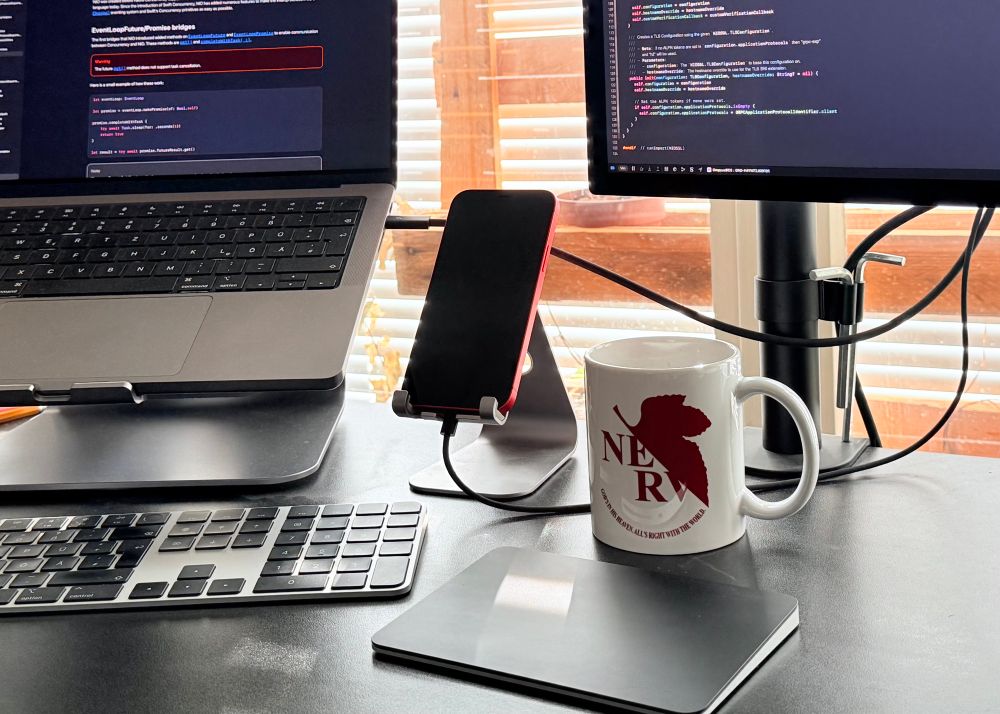 NERV coffee cup (from NGE) in front of some Macs doing Xcode junk. 