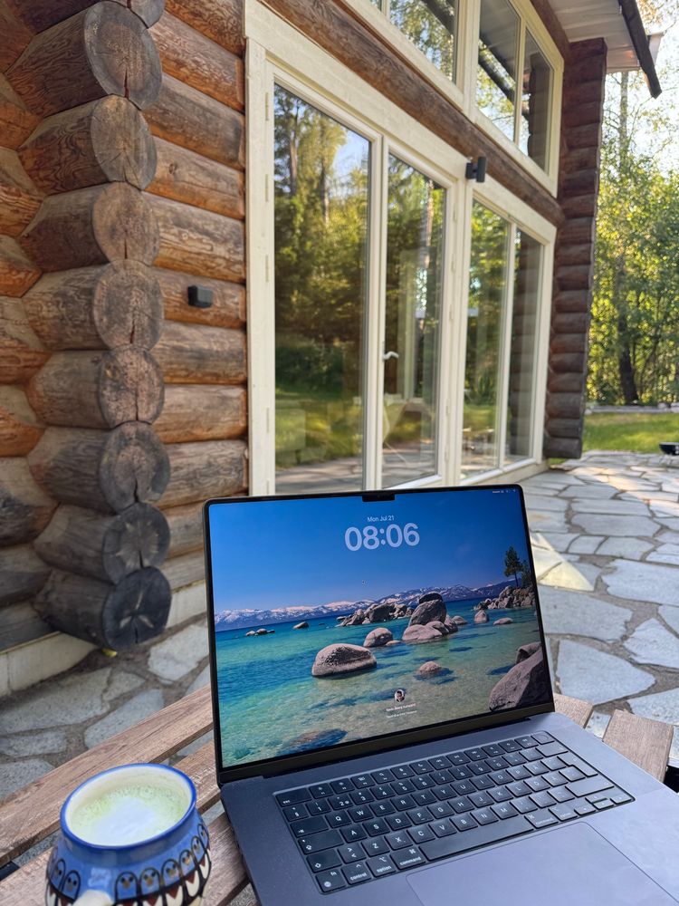 A cup of matcha and a MacBook on a table, overlooking a timber house