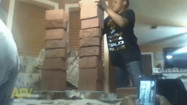 a boy wearing a black shirt that says gold on it is standing in front of a stack of bricks