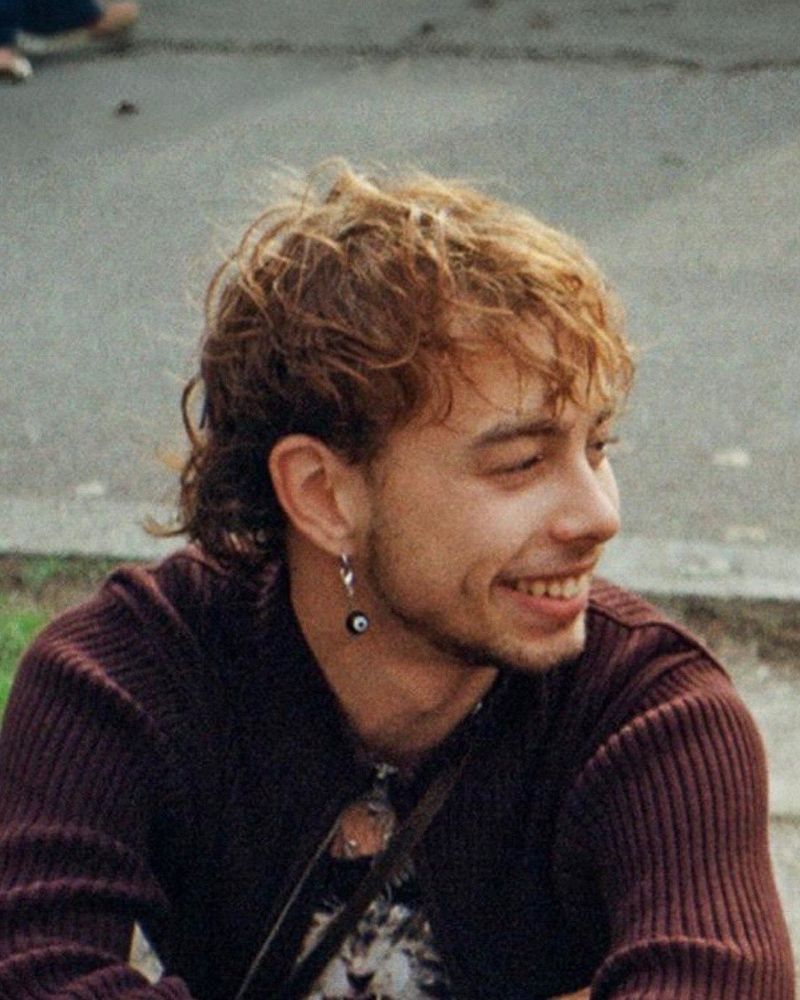 ein Mann mit lockigem Haar und Ohrring lächelnd