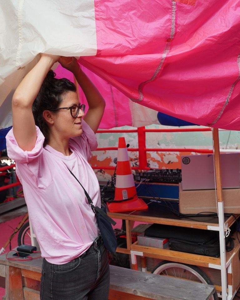 eine Frau hält ein großes pink- und gelbfarbenes Zelt hoch