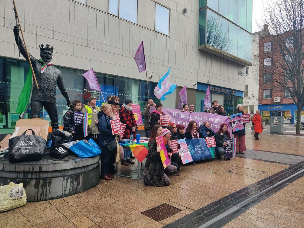 Group of people posing for a picture. People are holding various banners, placards and flags supporting women's equality and LGBTQ+ rights.