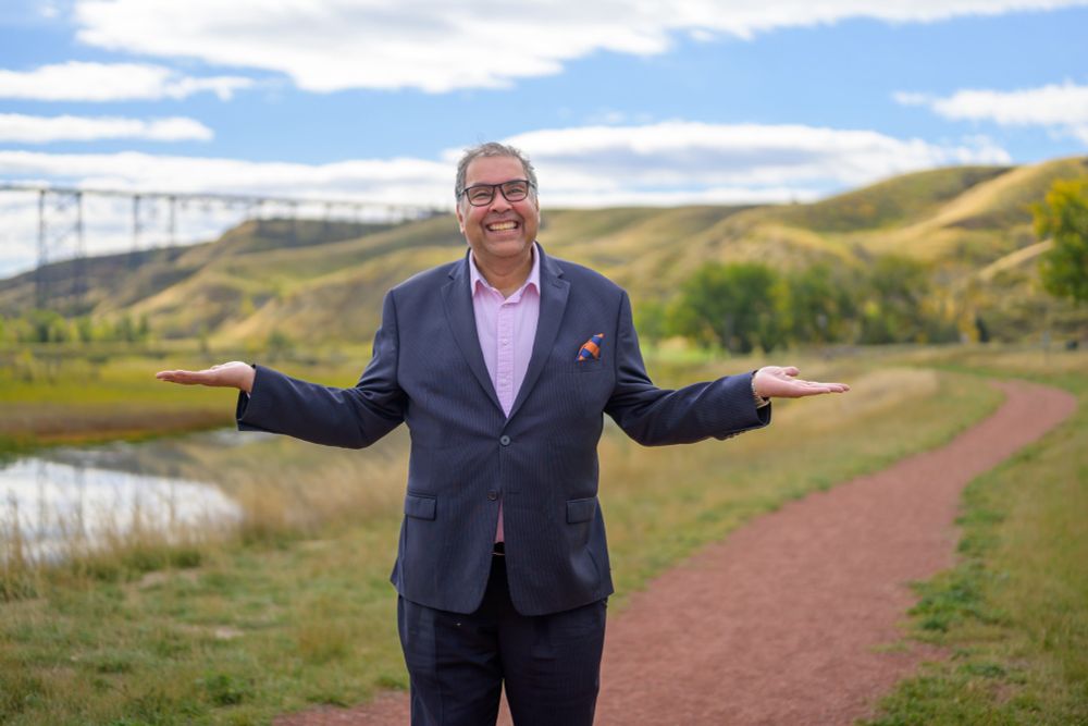 Naheed Nenshi standing in front of High Level bridge in Lethbridge under a big blue sky