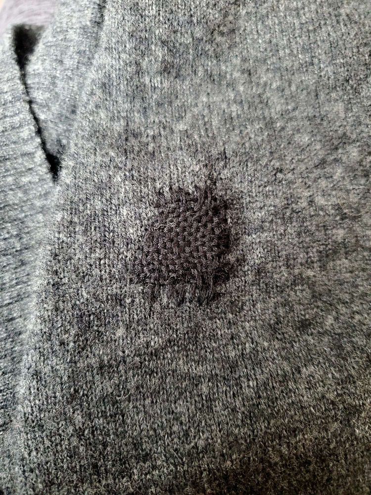 A Grey cardigan sleeve that had a hole in it that has been repaired with dark Grey thread via darning.