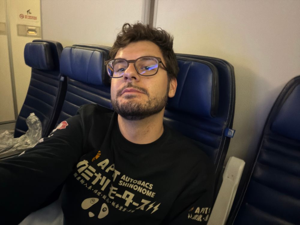 Adam sitting in a plane seat in a group of four that is otherwise empty.