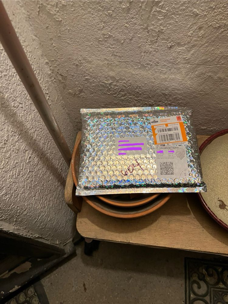 Iridescent bubble envelope on porch sits atop plant pots. Nighttime, light from above, address edited out. 