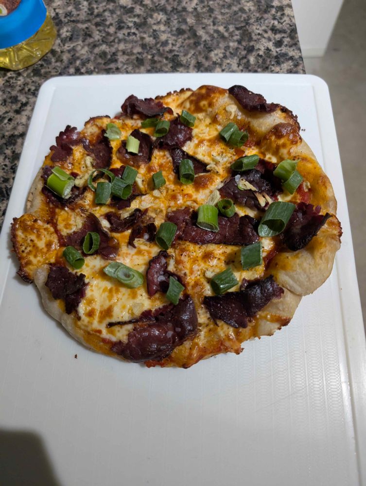 a sourdough pizza with smoked brisket, garlic, and green onion