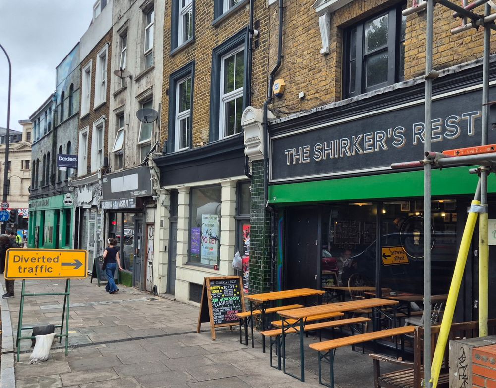 The exterior of the pub, the Shirker's Rest, with a road sign on the pavement outside reading "Diverted traffic" with an arrow conveniently pointing right at the pub.