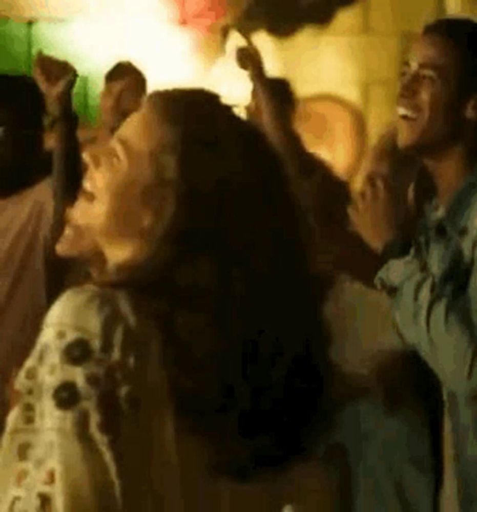 a woman is dancing in a crowd of people at a party while holding a fan in her hand .