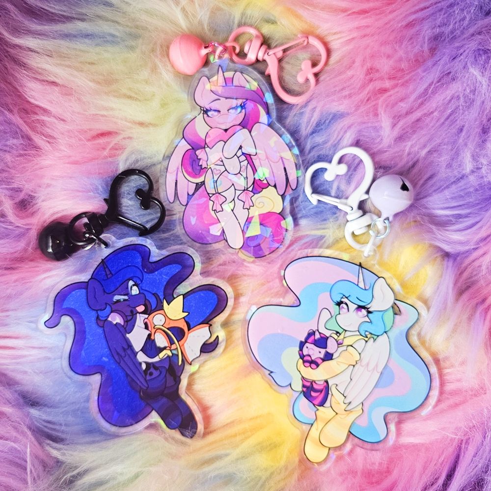 3 Acrylic Charms of MLP characters wearing socks. One is of Luna wearing a gamer themed outfit holding a Magikarp plushie. One is of Celestia wearing light yellow socks holding a Twilight plushie. And one is of Cadence in a more Lingerie esc outfit holding a heart. 