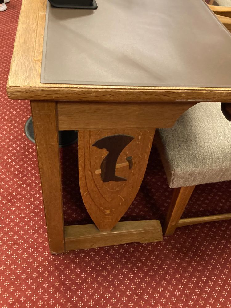 Die Seite eines Tisches ist mit Holzintarsien verziert, die einen Hammer und einen Arbeitsstiefel abbilden. 