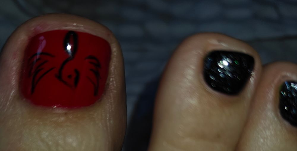 A black outline of a Phoenix on red polish. Next to black-smokey glittery polish 