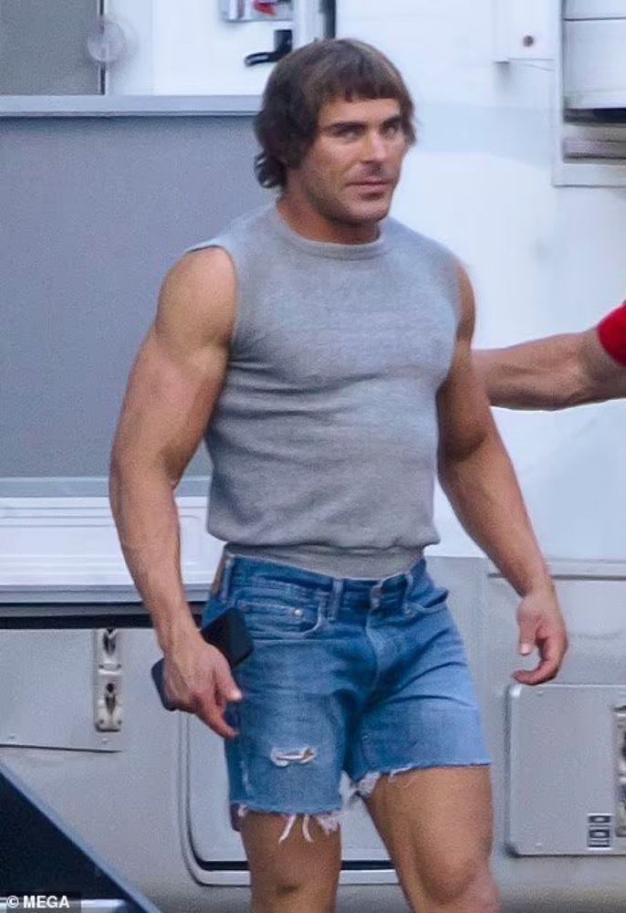 zac efron with bangs in denim cutoffs and a sleeveless gray sweatshirt 