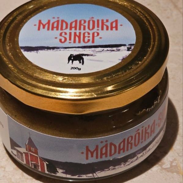A small jar which says mädarõika-sinep against a backdrop of a bleak landscape.