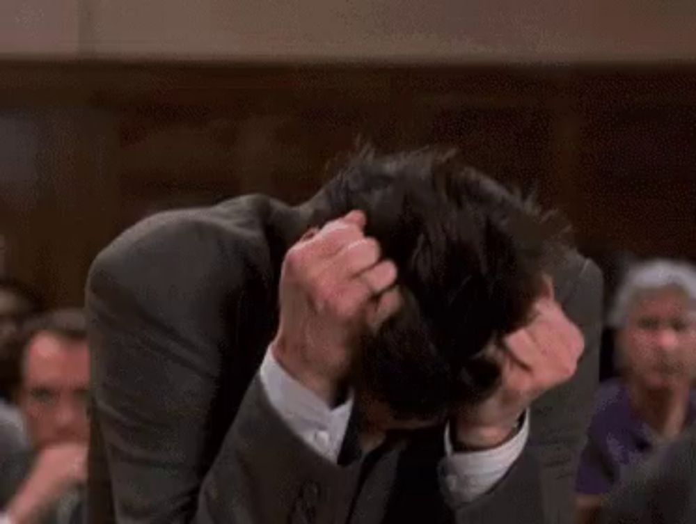 a man in a suit and tie is scratching his head while standing in front of a crowd .