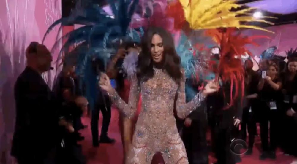 a woman in a colorful costume is dancing on a red carpet in front of a crowd of people .